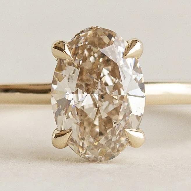 Oval champagne diamond held by four prongs on a slim yellow-colored band