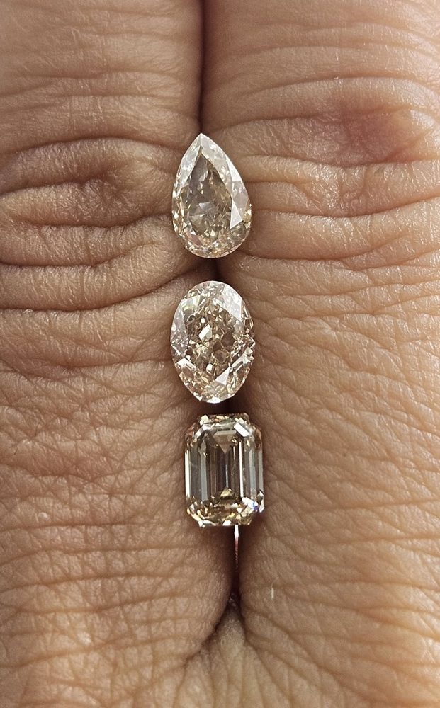 Three warm diamonds with pear, oval and rectangular outlines resting on a hand