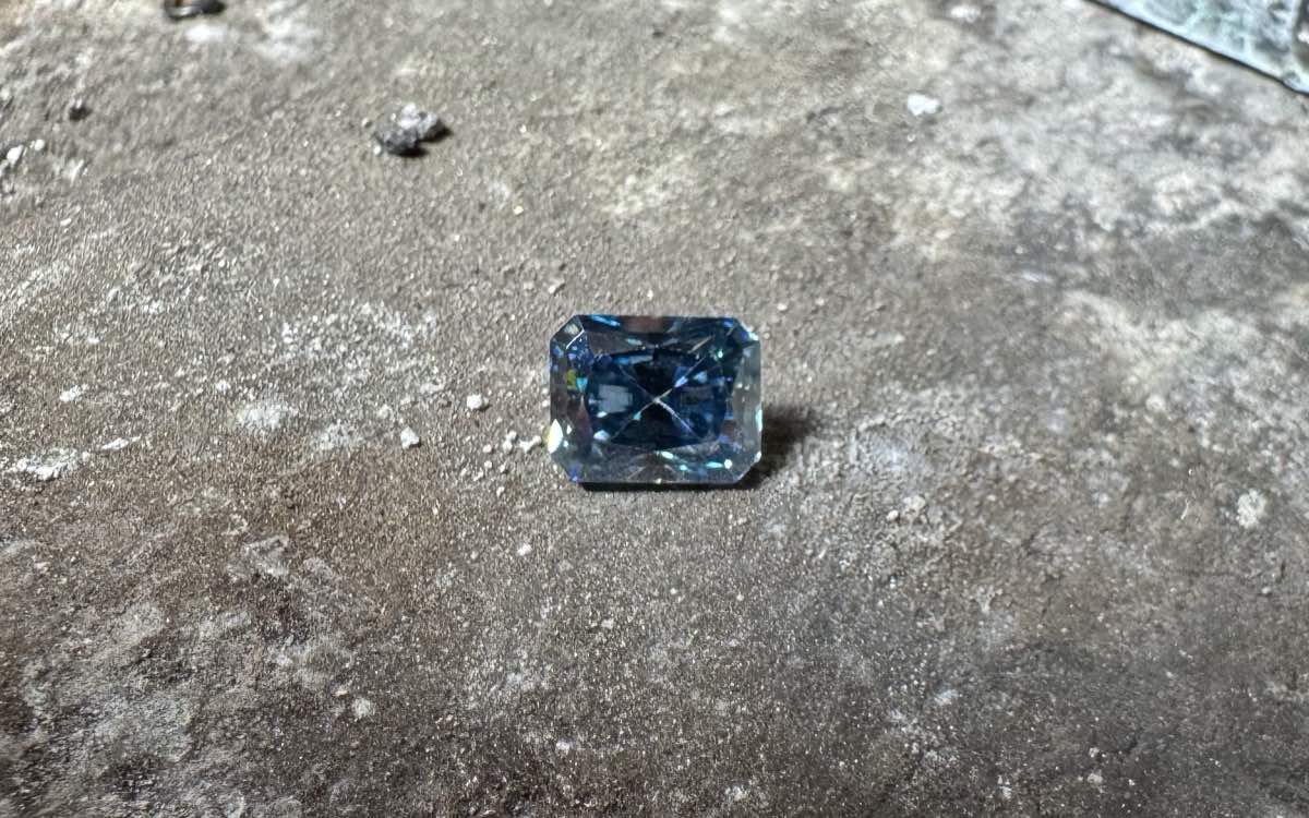 The blue eBay stone face up on a worn metal bench, showing a vivid, even blue with no visible sign of the coating.