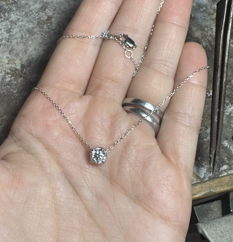 White gold diamond solitaire necklace resting in a hand at the jewelry bench.