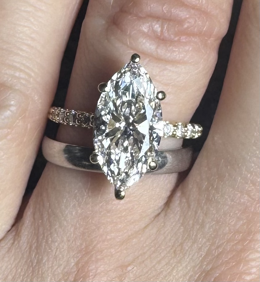 The finished 3ct marquise engagement ring shown on a hand beside a plain band.